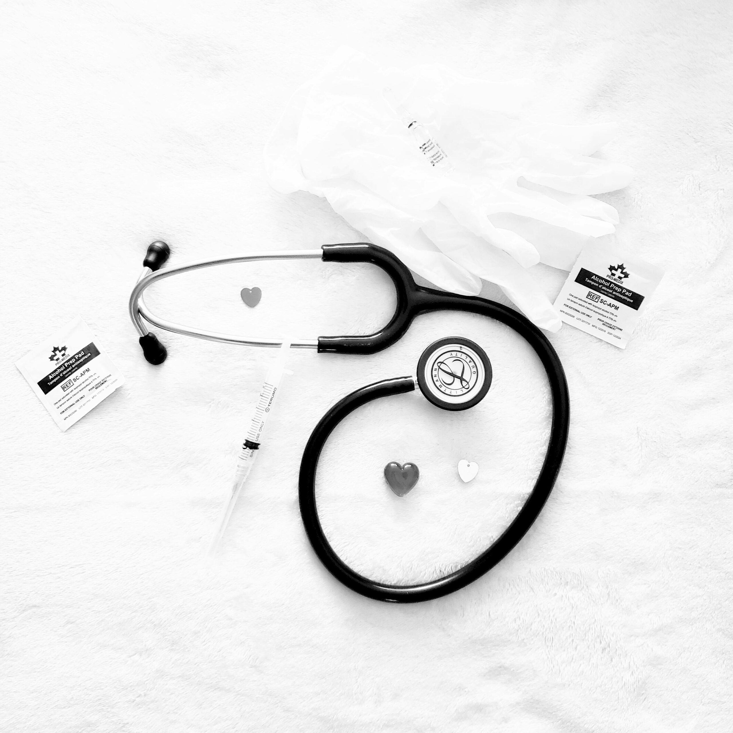 Black and white image of stethoscope and medical tools arranged on a white surface, symbolizing healthcare.
